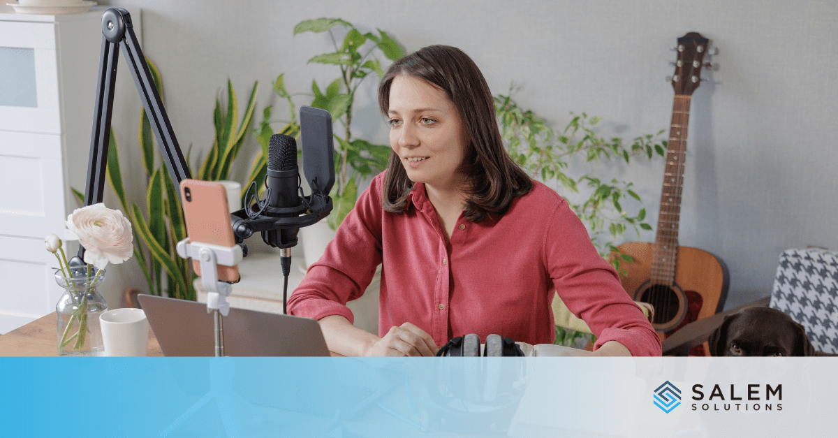 A woman at her desk is recording a video resume using a laptop and microphone.