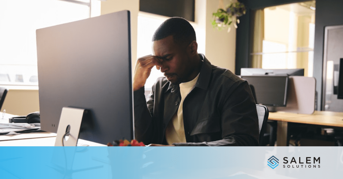 A man feeling stressed at work, sitting in front of a computer screen in an office setting.