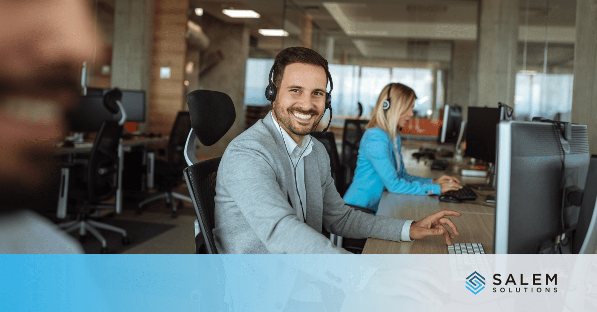 Office workers at desks with headsets, smiling and communicating in a modern workspace.