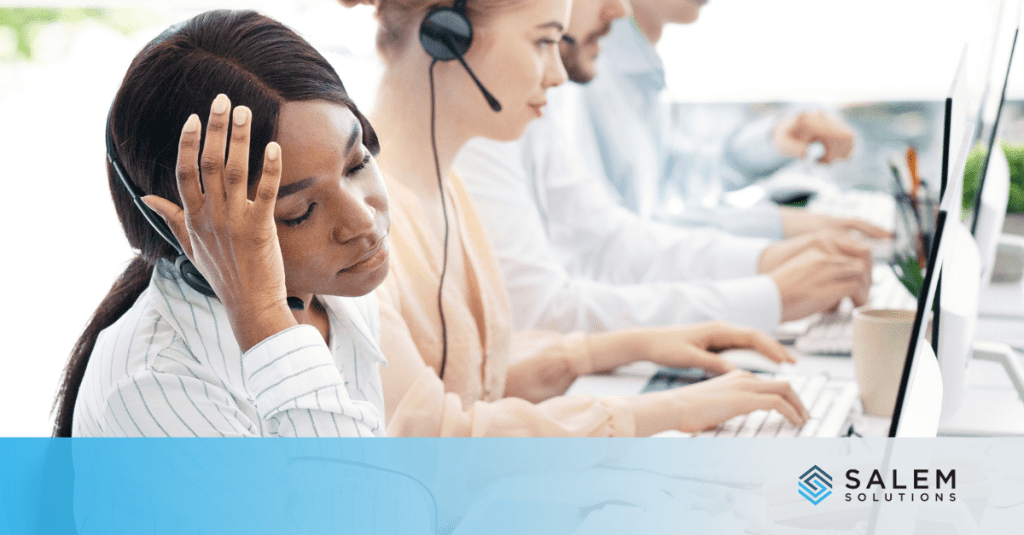 A woman at a desk, head in hands, depicting the stress of call center work and the need for effective stress management strategies.
