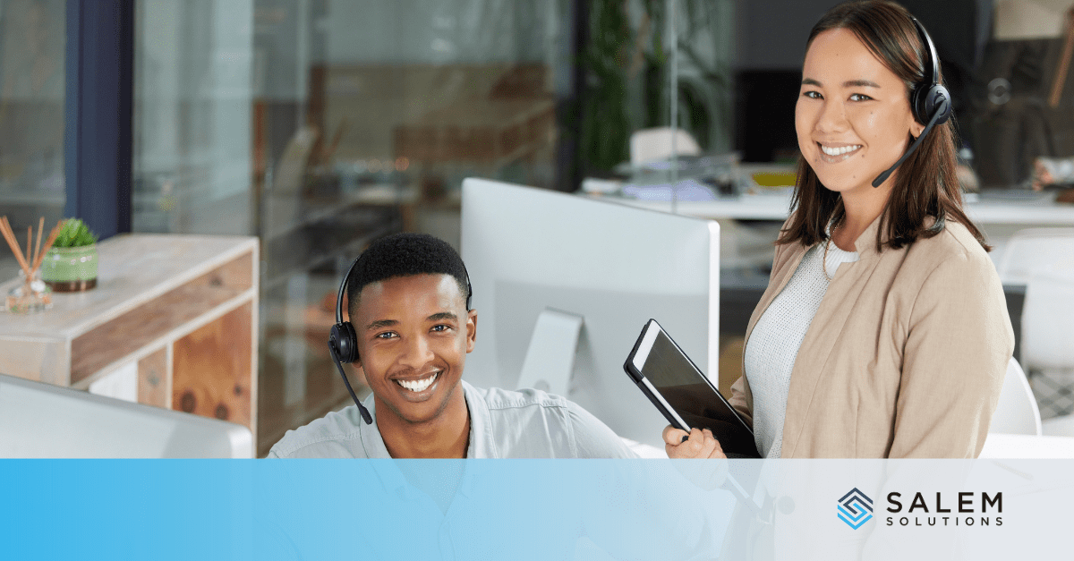 Two professionals in an office collaborate, one wearing a headset at a computer and the other holding a tablet, discussing temp-to-hire staffing strategies.
