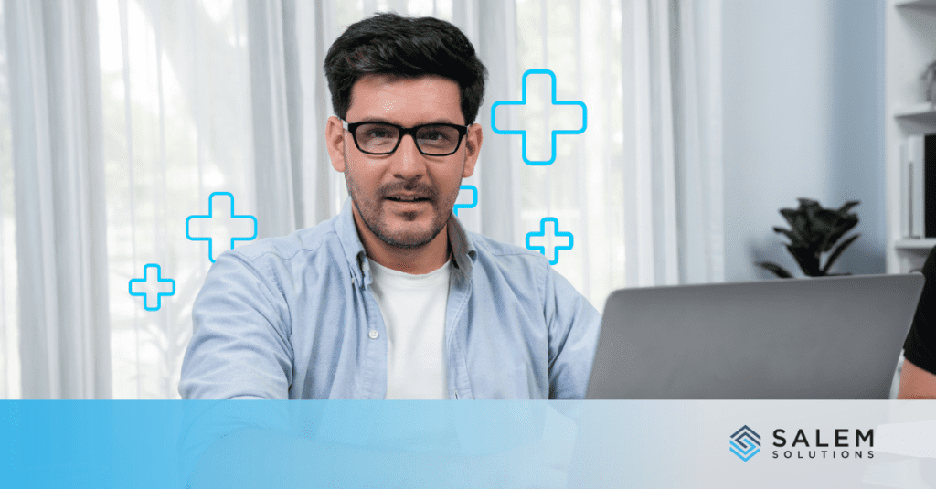 Professional man with glasses working on laptop in modern office with healthcare cross icons, representing healthcare call center careers.